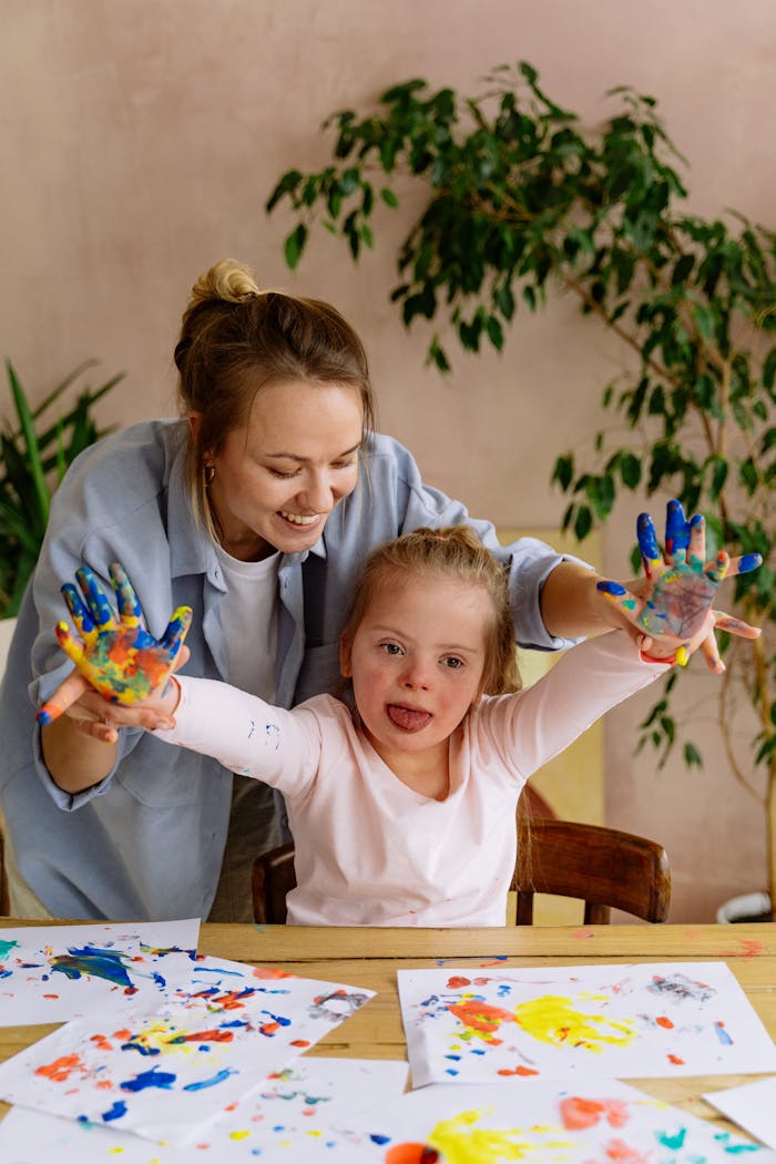 A joyful moment between a mother and daughter painting with colorful handprints indoors.