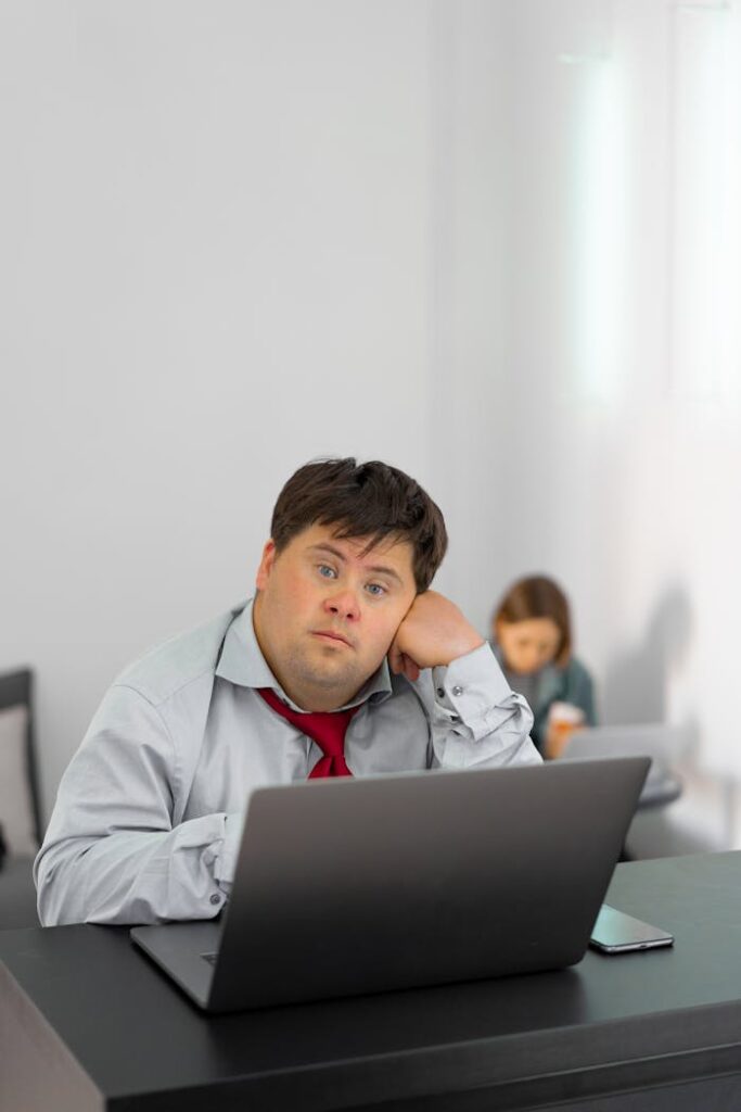 pexels-photo-7698285 A man with Down syndrome sitting at a desk using a laptop in an office setting.