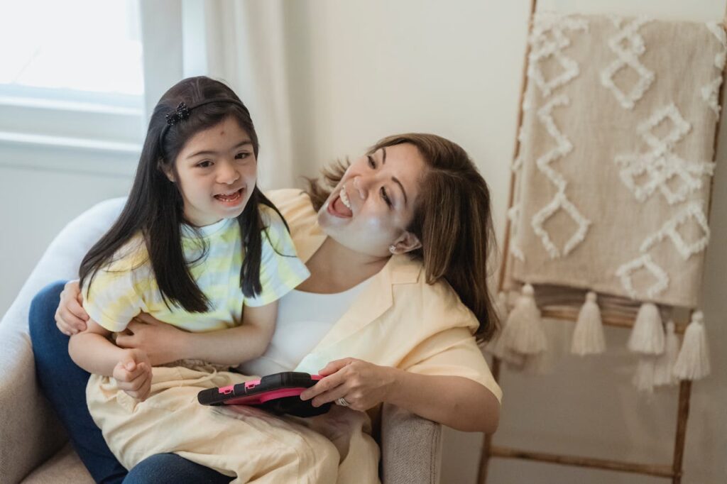 pexels-photo-7943275 A joyful mother and daughter bonding while using a tablet, seated indoors.