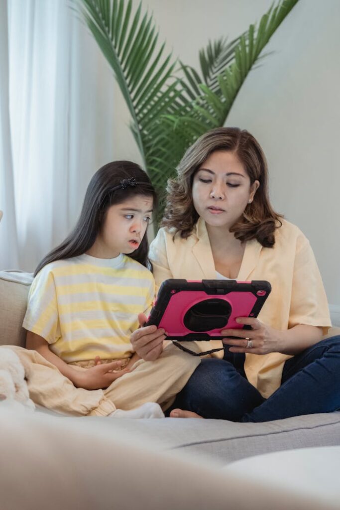 pexels-photo-7943949 A mother and daughter sitting together using a digital tablet indoors. Family bonding time.